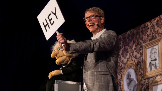 Bauchredner Jörg Jará hält ein Schild mit der Aufschrift HEY hoch